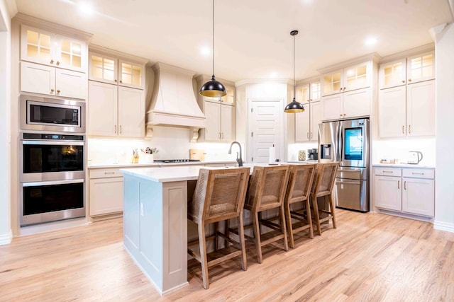 kitchen featuring appliances with stainless steel finishes, a breakfast bar, hanging light fixtures, custom range hood, and a center island with sink