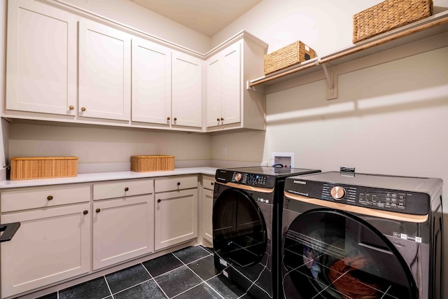 clothes washing area featuring cabinets, washer and dryer, and dark tile patterned floors