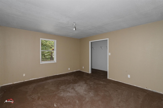 unfurnished bedroom with dark carpet, a closet, a textured ceiling, and a walk in closet