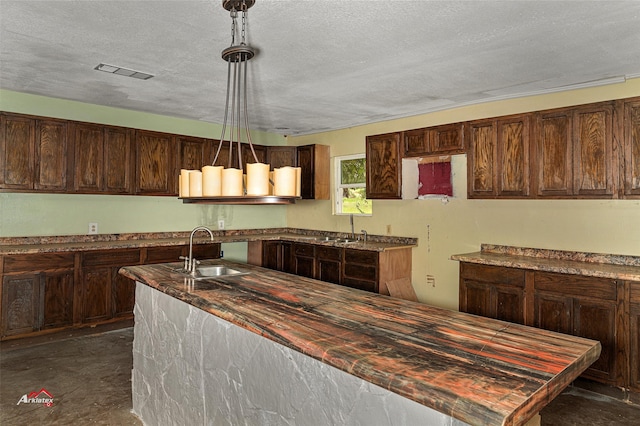 kitchen with a textured ceiling, dark brown cabinetry, sink, and pendant lighting