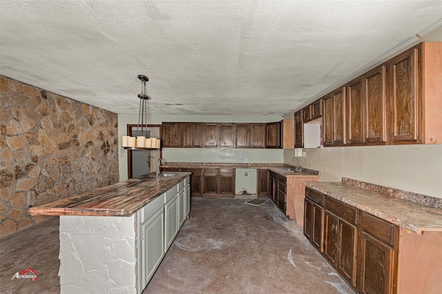 kitchen featuring a textured ceiling, hanging light fixtures, a kitchen island with sink, and sink