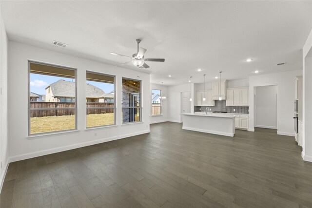 unfurnished living room featuring a sink, a healthy amount of sunlight, ceiling fan, and dark wood-style flooring