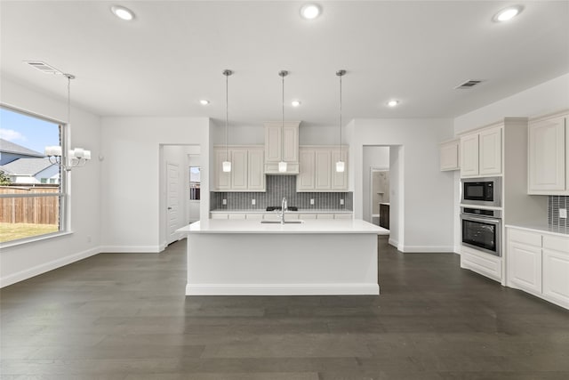 kitchen featuring visible vents, a sink, decorative backsplash, black microwave, and stainless steel oven