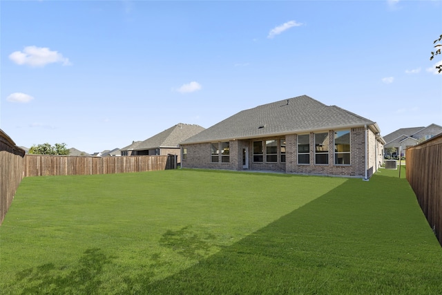 rear view of property featuring brick siding, roof with shingles, a fenced backyard, and a lawn