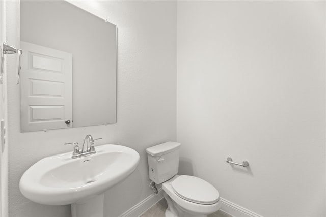 half bathroom with a sink, baseboards, and toilet