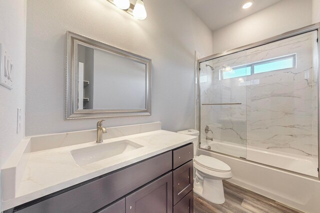 full bathroom featuring vanity, hardwood / wood-style flooring, enclosed tub / shower combo, and toilet