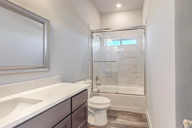 full bathroom featuring hardwood / wood-style floors, toilet, vanity, and bath / shower combo with glass door