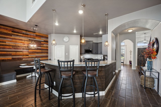 kitchen featuring wooden walls, light stone countertops, dark hardwood / wood-style floors, gray cabinetry, and a kitchen bar