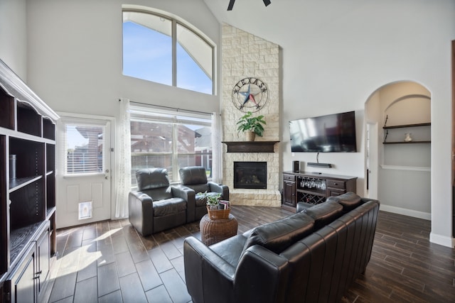 living room with ceiling fan, a stone fireplace, dark hardwood / wood-style floors, and high vaulted ceiling