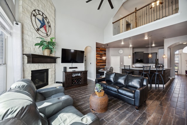 living room with ceiling fan, high vaulted ceiling, dark hardwood / wood-style flooring, and a stone fireplace