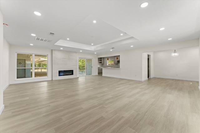 unfurnished living room featuring a fireplace, a raised ceiling, and light hardwood / wood-style floors