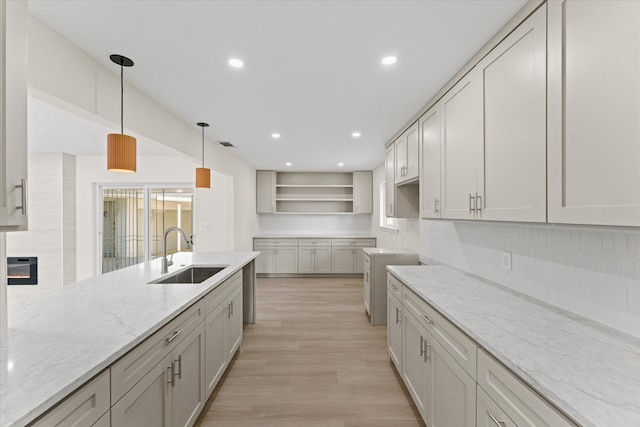 kitchen with light hardwood / wood-style floors, white cabinets, light stone countertops, decorative light fixtures, and sink