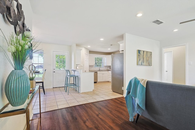 kitchen featuring light wood-type flooring, decorative backsplash, stainless steel appliances, white cabinets, and a kitchen bar