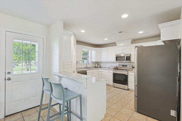 kitchen with kitchen peninsula, a wealth of natural light, stainless steel appliances, and white cabinets