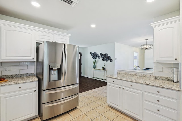 kitchen with light wood-type flooring, tasteful backsplash, stainless steel fridge, hanging light fixtures, and white cabinetry