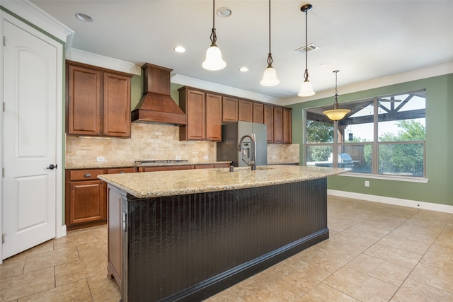 kitchen featuring custom range hood, an island with sink, light stone counters, pendant lighting, and sink