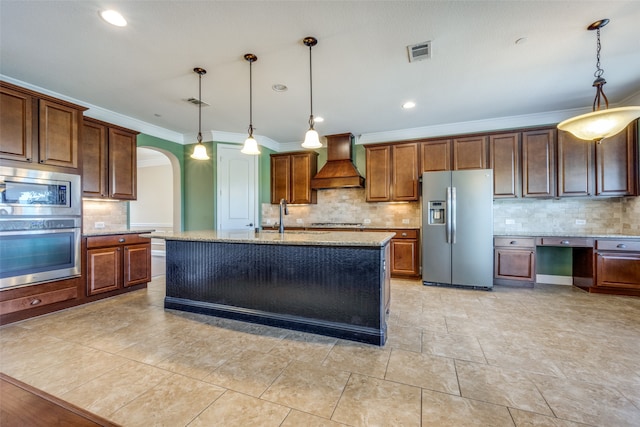 kitchen featuring hanging light fixtures, light stone countertops, stainless steel appliances, custom exhaust hood, and a kitchen island with sink