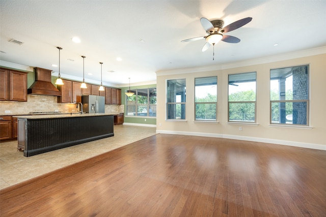 kitchen with a kitchen island with sink, light wood-type flooring, custom range hood, and a healthy amount of sunlight