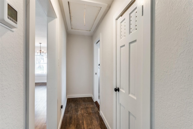 hallway featuring dark wood-style floors, a textured wall, attic access, and baseboards