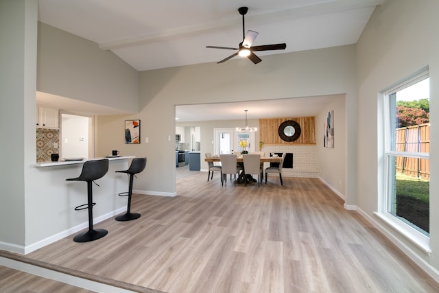 dining area featuring ceiling fan with notable chandelier, light wood-type flooring, vaulted ceiling, and a healthy amount of sunlight