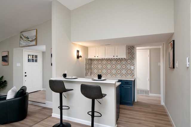 kitchen featuring blue cabinets, white cabinets, a kitchen bar, light hardwood / wood-style floors, and decorative backsplash