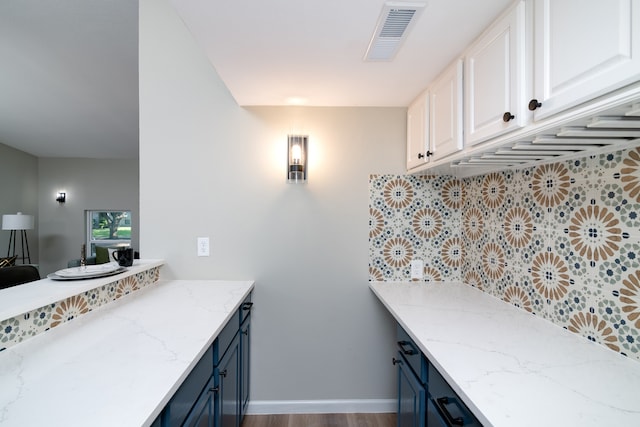 kitchen with blue cabinetry, light stone countertops, hardwood / wood-style floors, and white cabinetry