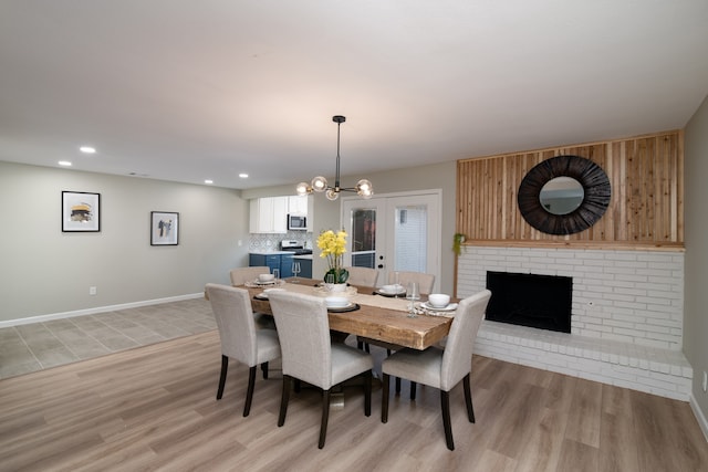 dining area with french doors, light wood-type flooring, a fireplace, and a chandelier