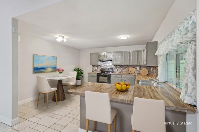 kitchen featuring decorative backsplash, a breakfast bar, kitchen peninsula, black electric range oven, and sink