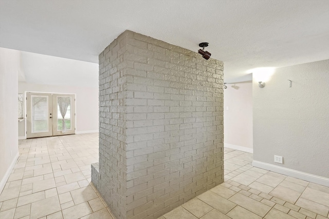 unfurnished room featuring a textured ceiling, light tile patterned floors, french doors, and brick wall