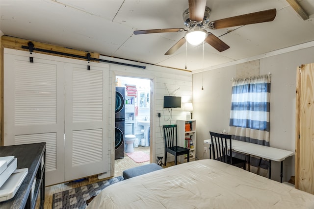 bedroom with ceiling fan, connected bathroom, stacked washing maching and dryer, a closet, and a barn door