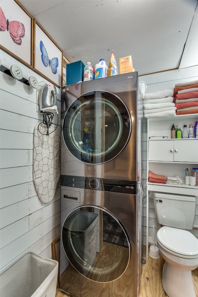 laundry room featuring stacked washer / drying machine, wood walls, and light wood-type flooring