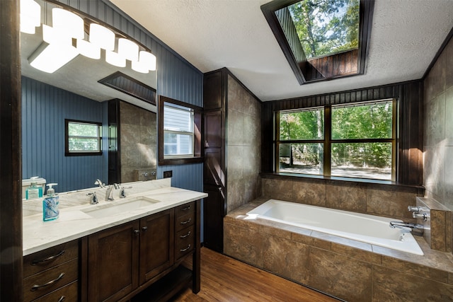 bathroom featuring a wealth of natural light, tiled tub, wood-type flooring, and vanity