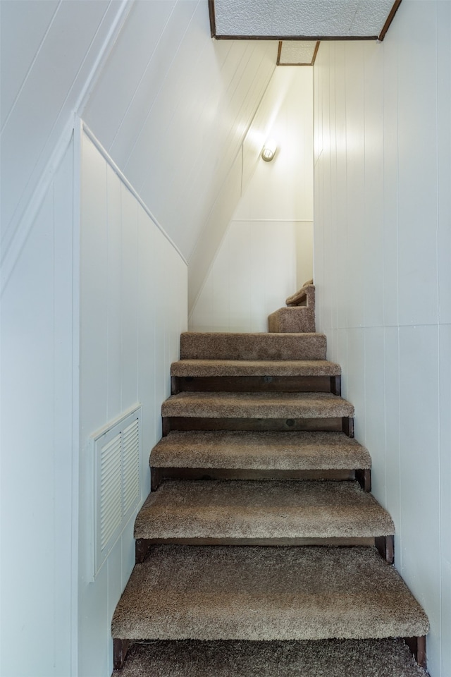 stairway featuring lofted ceiling and wood walls