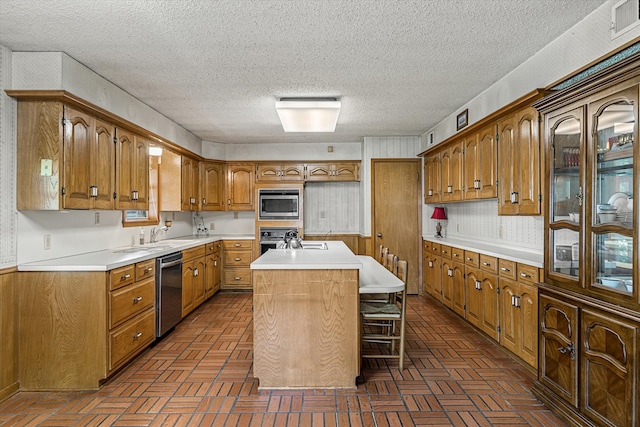 kitchen featuring an island with sink, stainless steel appliances, a textured ceiling, and a kitchen breakfast bar