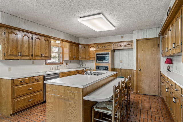 kitchen featuring appliances with stainless steel finishes, a kitchen breakfast bar, an island with sink, a textured ceiling, and sink