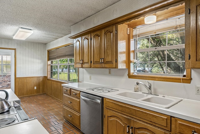 kitchen featuring a textured ceiling, stainless steel dishwasher, wooden walls, and sink