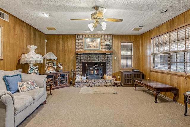 carpeted living room featuring wood walls, ceiling fan, a fireplace, and a textured ceiling