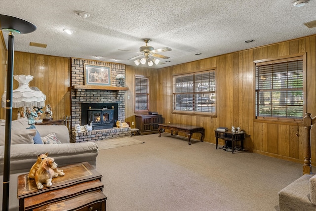 carpeted living room featuring a textured ceiling, wood walls, ceiling fan, and a brick fireplace