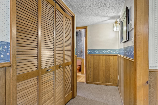 hallway featuring a textured ceiling, wood walls, and light colored carpet