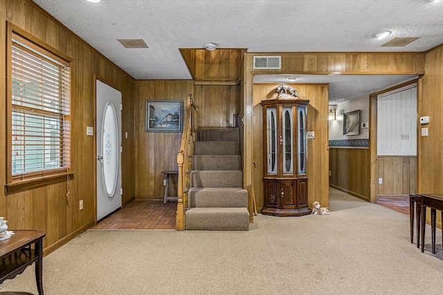 foyer entrance featuring a textured ceiling, wood walls, and carpet