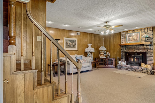 carpeted living room featuring a brick fireplace, ceiling fan, a textured ceiling, and wooden walls