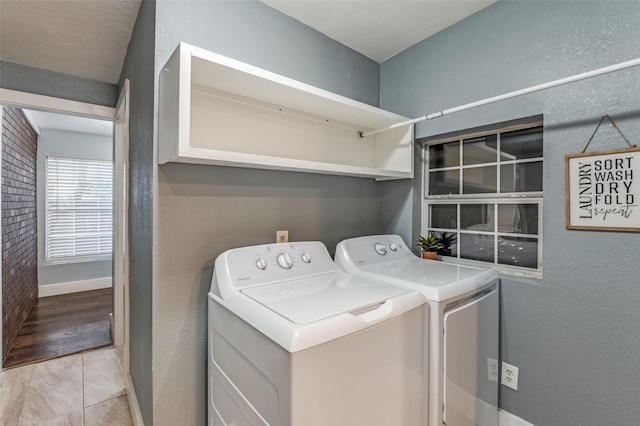 clothes washing area featuring a textured wall, laundry area, washing machine and clothes dryer, and baseboards