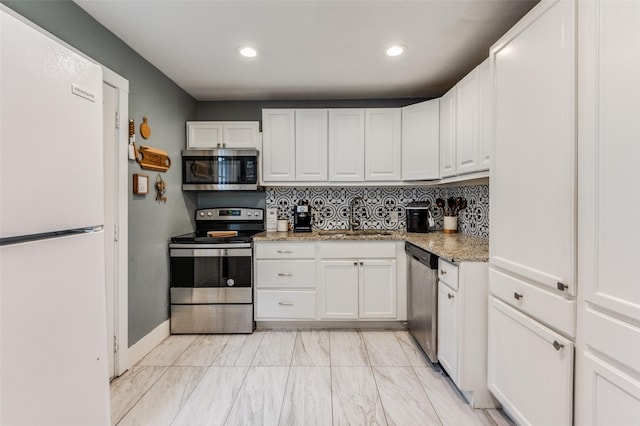 kitchen featuring light stone counters, stainless steel appliances, a sink, white cabinets, and backsplash