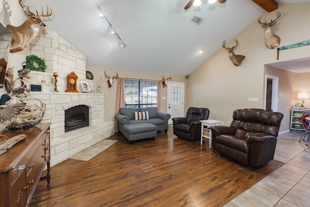 living room with ceiling fan, rail lighting, vaulted ceiling with beams, wood-type flooring, and a fireplace