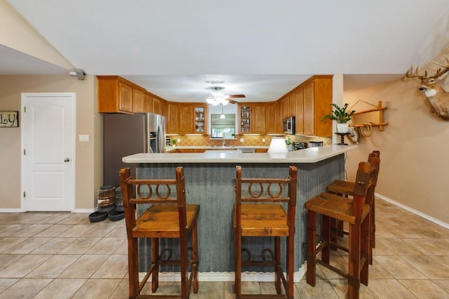 kitchen with light tile patterned floors, a breakfast bar, backsplash, stainless steel appliances, and kitchen peninsula