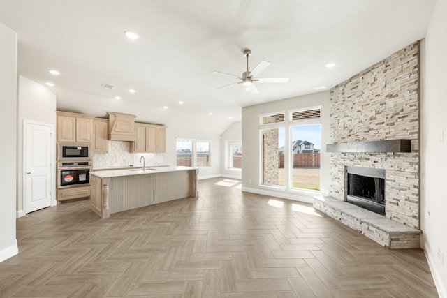 kitchen featuring premium range hood, light brown cabinetry, black microwave, an island with sink, and oven