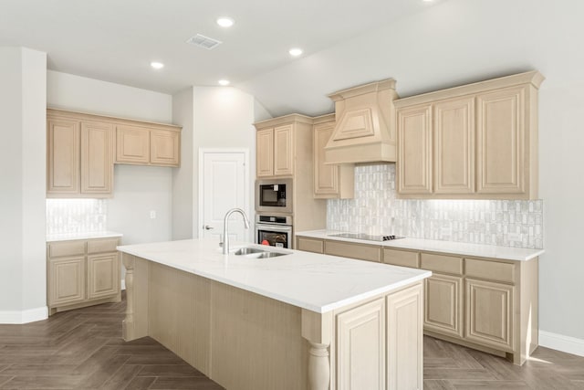 kitchen featuring built in microwave, sink, custom range hood, oven, and a kitchen island with sink