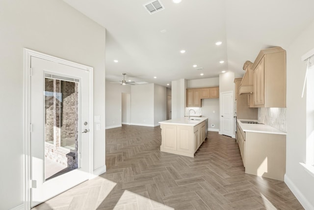 kitchen with parquet flooring, light brown cabinetry, sink, backsplash, and a center island with sink