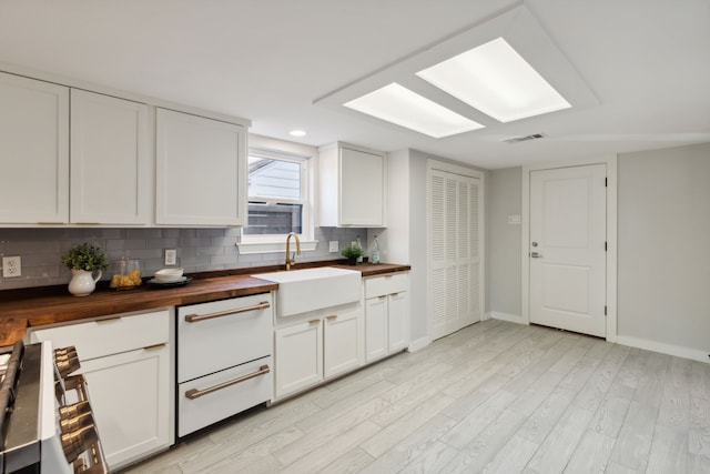 kitchen featuring sink, tasteful backsplash, light hardwood / wood-style flooring, stainless steel stove, and butcher block counters