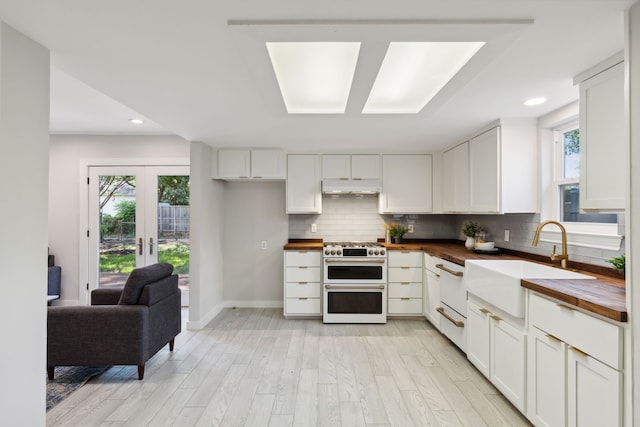 kitchen featuring white cabinets, high end stove, sink, and wooden counters